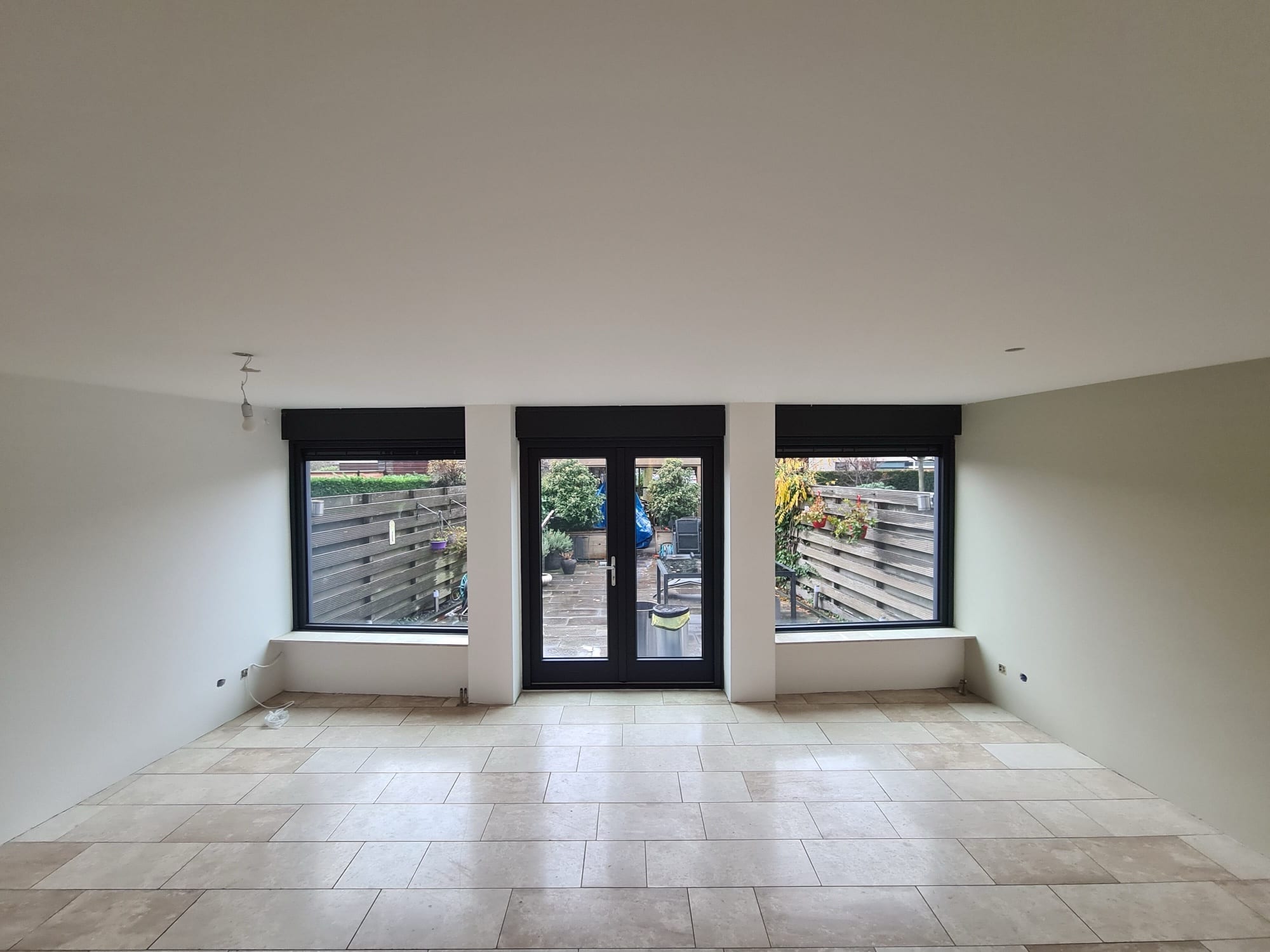 Strak afgewerkte woonkamer met openslaande tuindeuren, wanden en plafond gestuukt