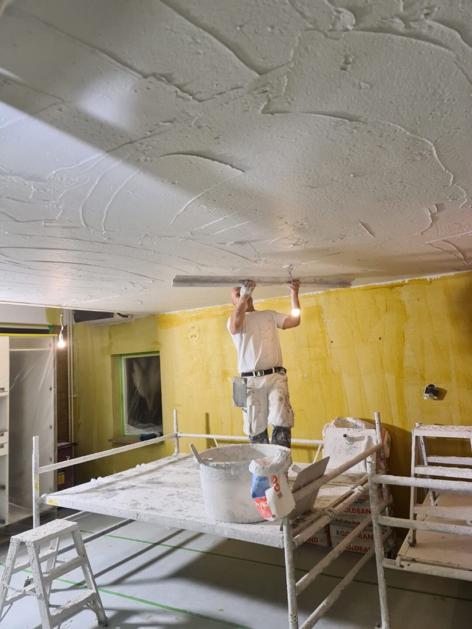 Stukadoor raapt vanaf de steiger een plafond, de verse laag moet nog drogen
