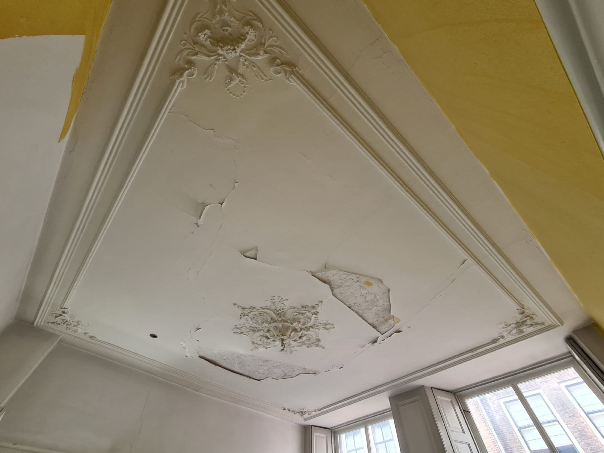 Ornamentenplafond met loszittend en gescheurd stucwerk voor het herstel