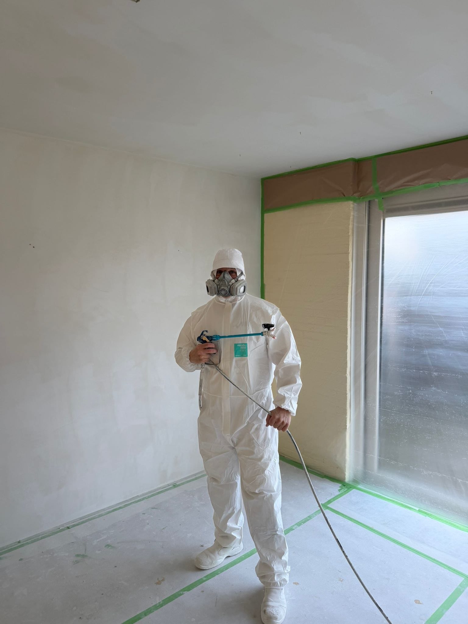 Stukadoor spuit de bovenhoek van een kamer, kozijnen afgeplakt met folie