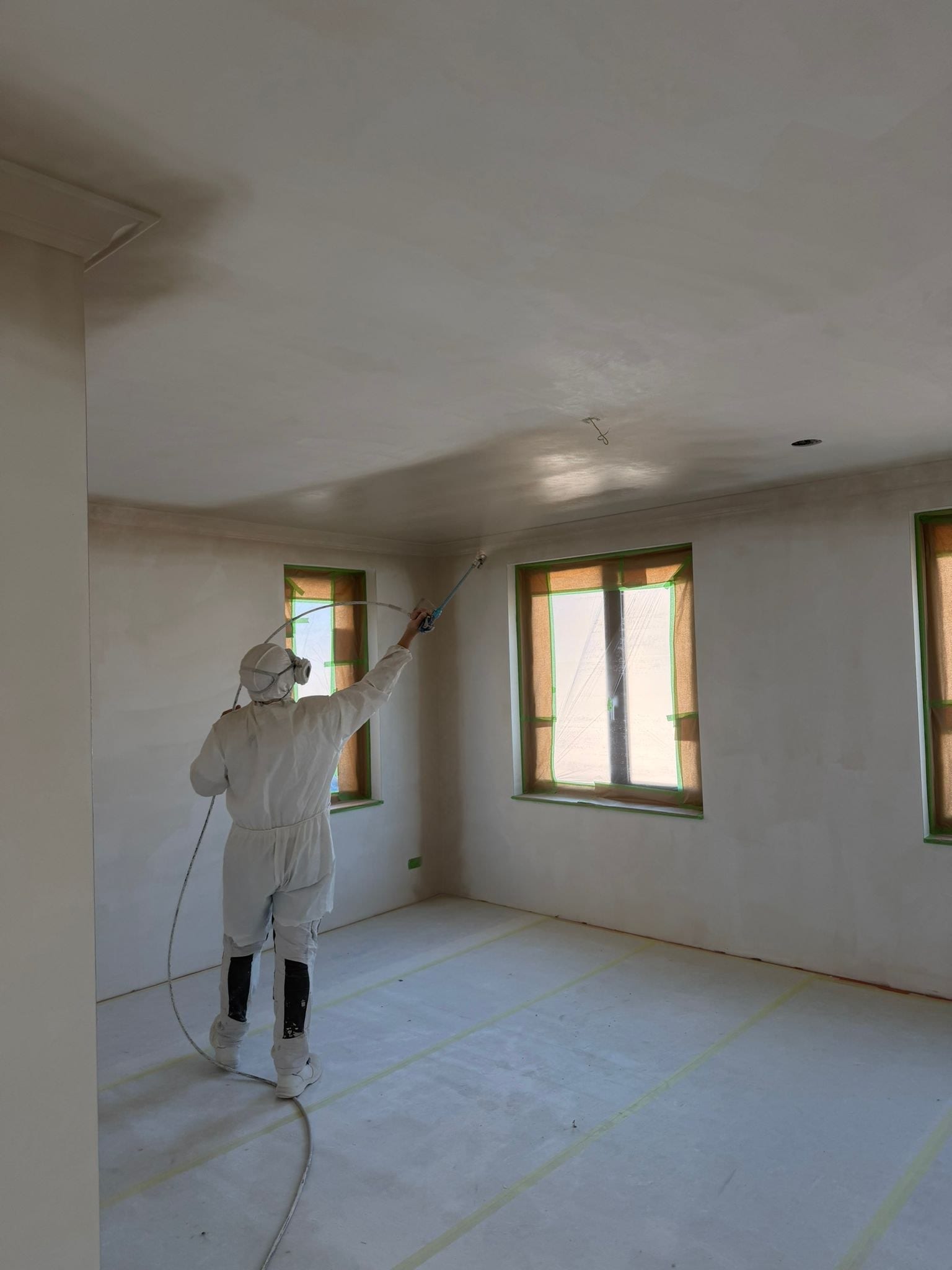 Stukadoor in beschermpak spuit met de airless installatie het plafond van een afgeplakte woonkamer