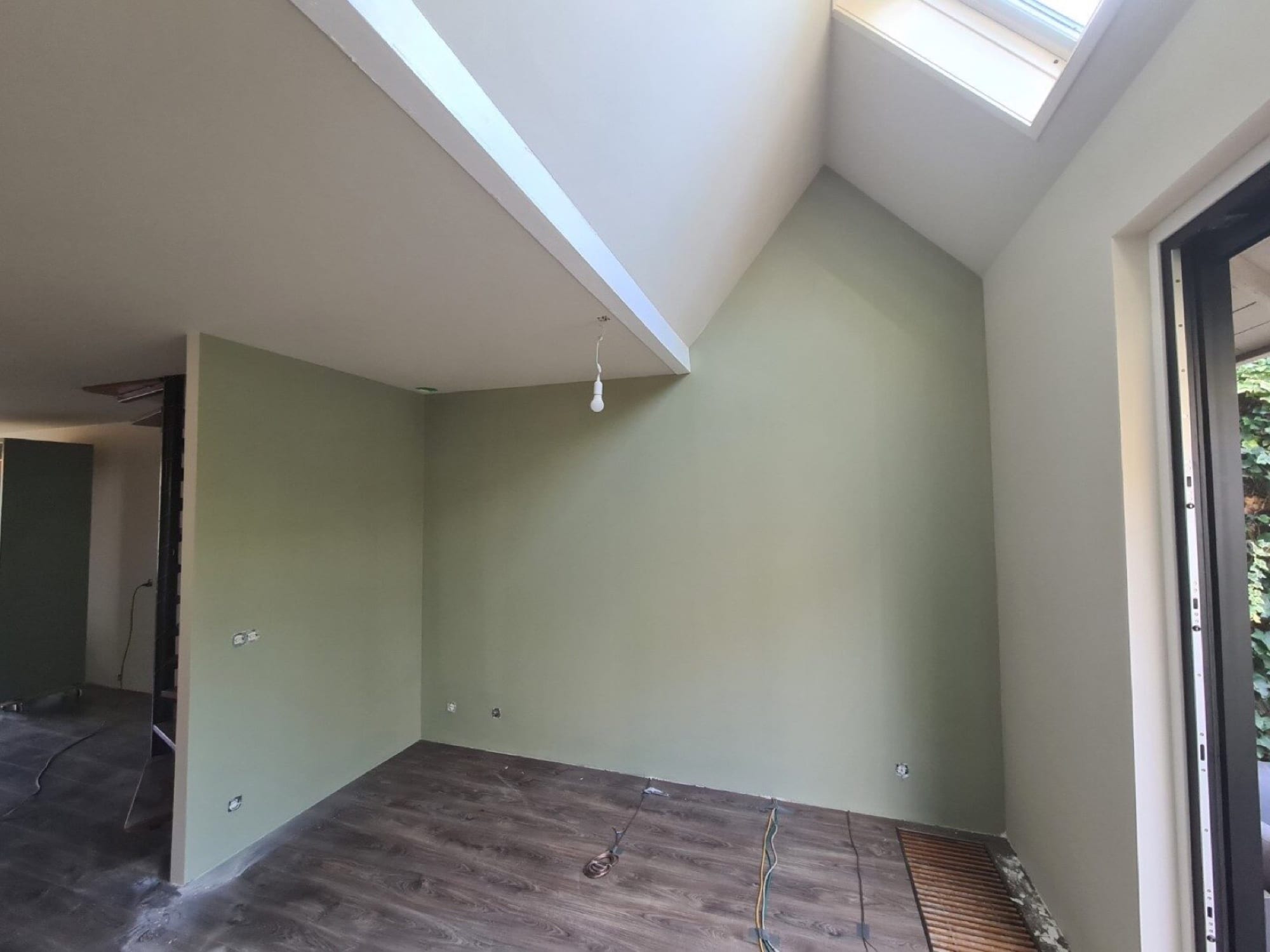 Groene accentwand onder een hoge vide met dakraam
