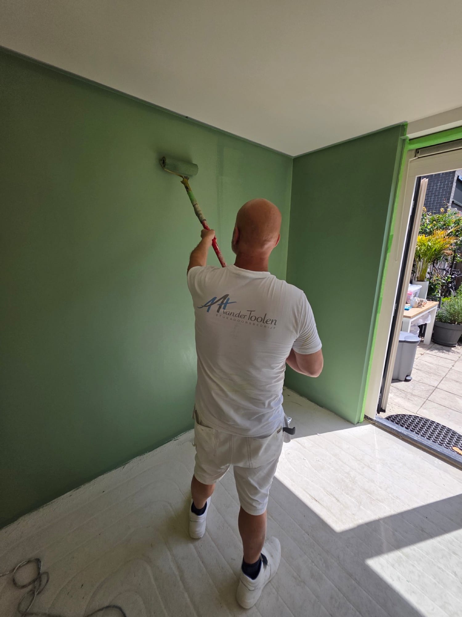 Stukadoor in bedrijfsshirt saust een groene accentwand in een woonkamer