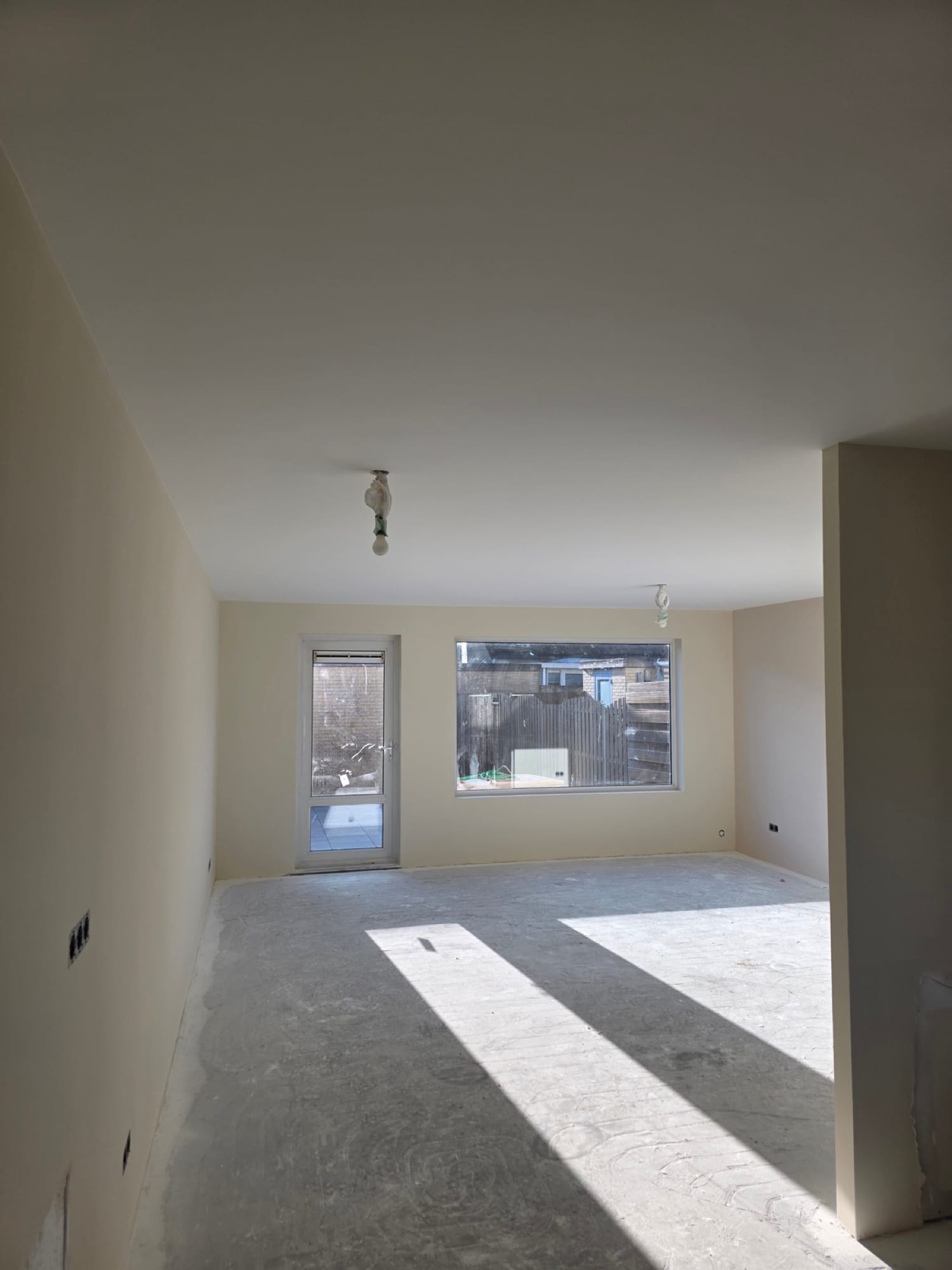 Lichte woonkamer met strak gestucte wanden en plafond, zonlicht door de tuindeur