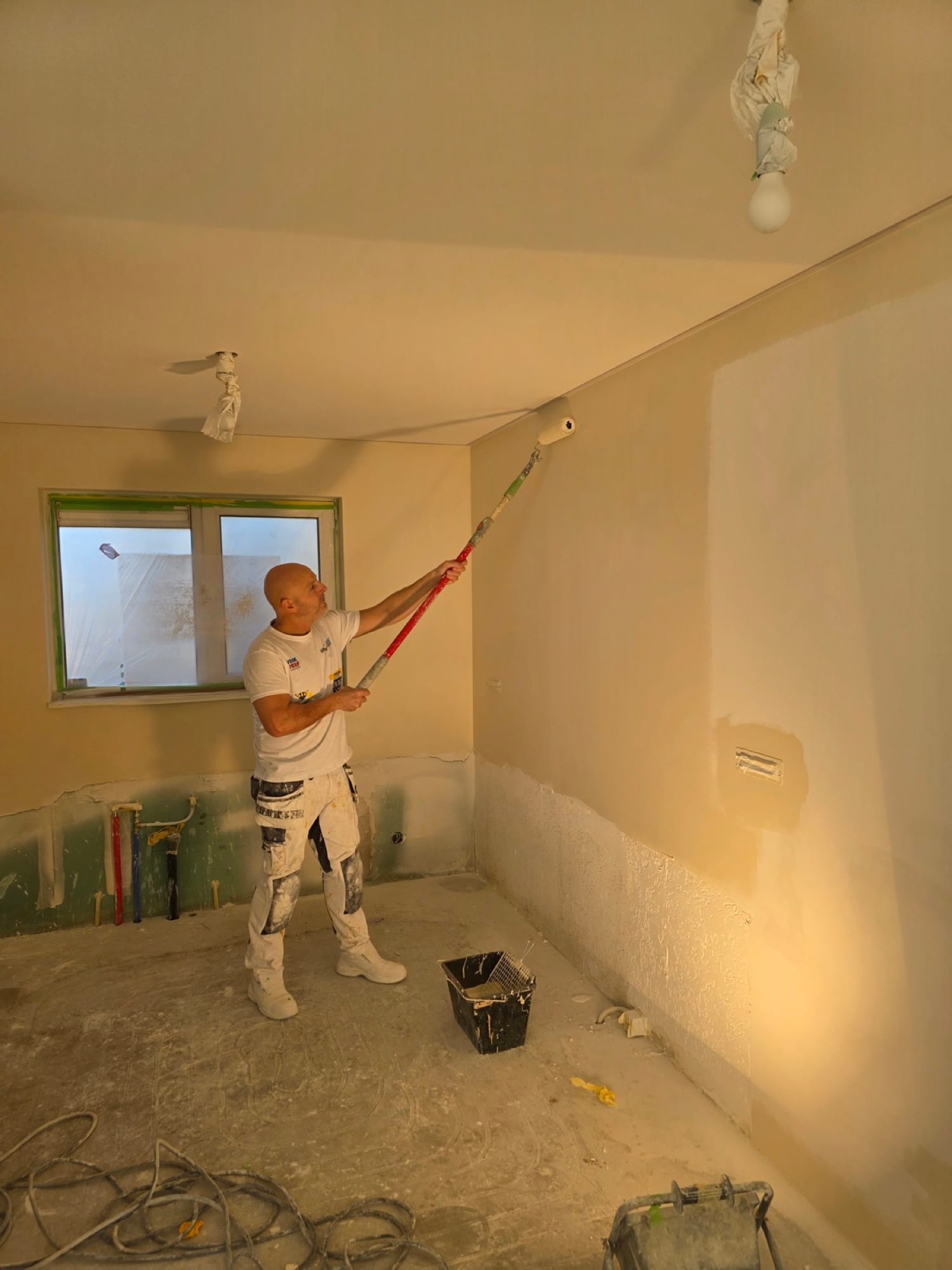 Stukadoor saust met een verlengde roller een strak gestucte wand in warm avondlicht