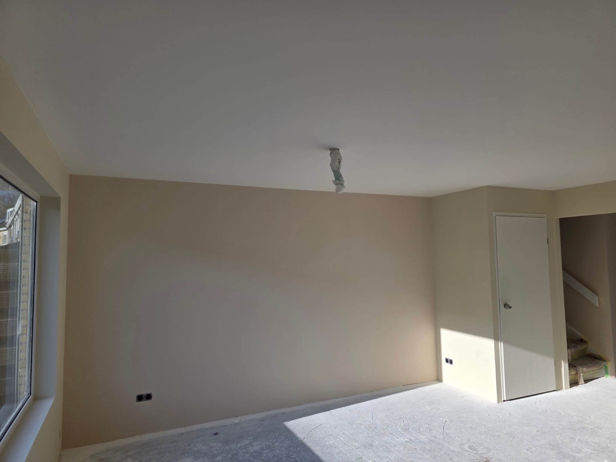 Strak gestucte woonkamerwand met zonlicht door een groot raam