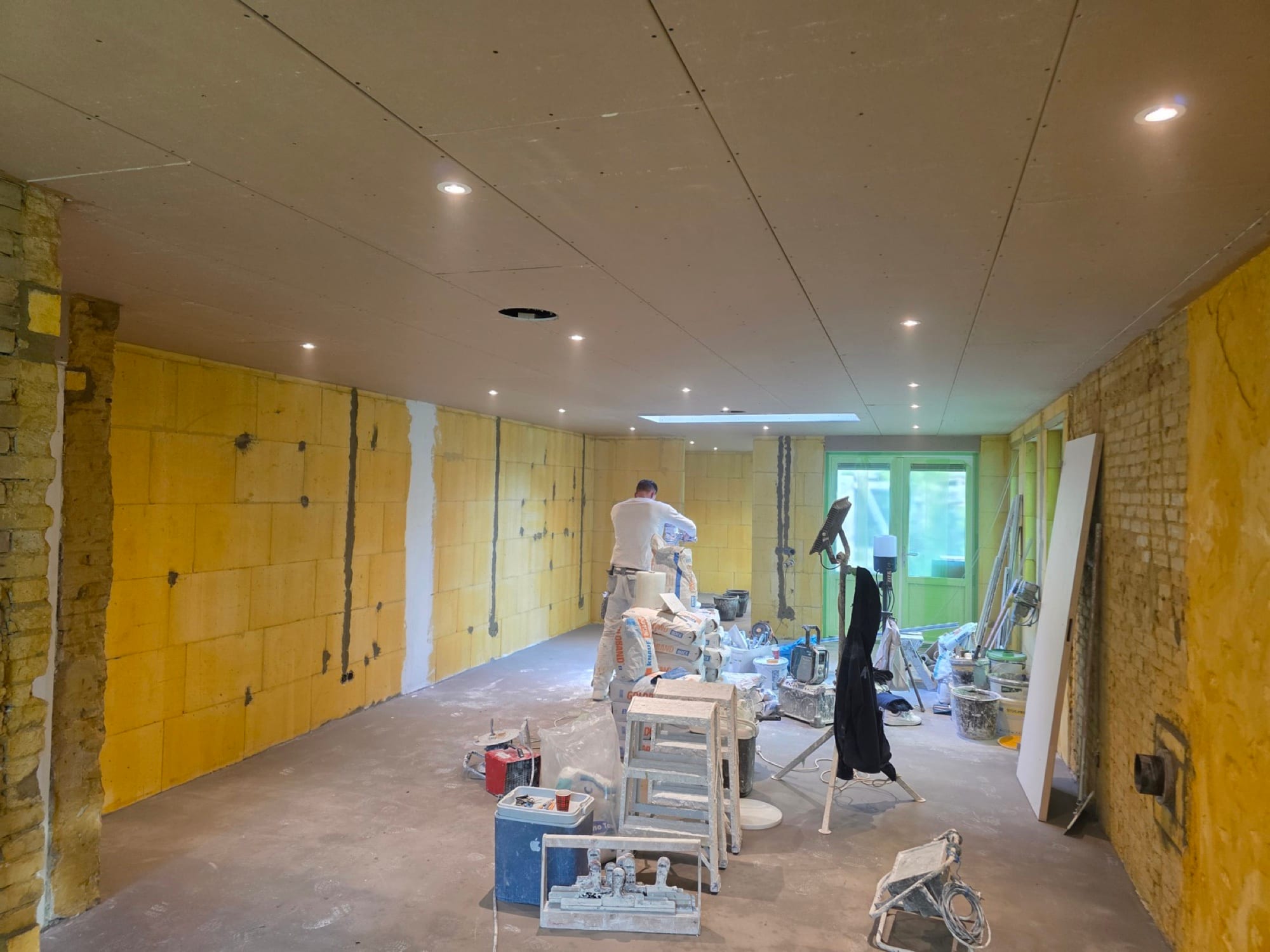 Stukadoor bereidt materiaal voor in een ruimte met nog onafgewerkte gele wanden