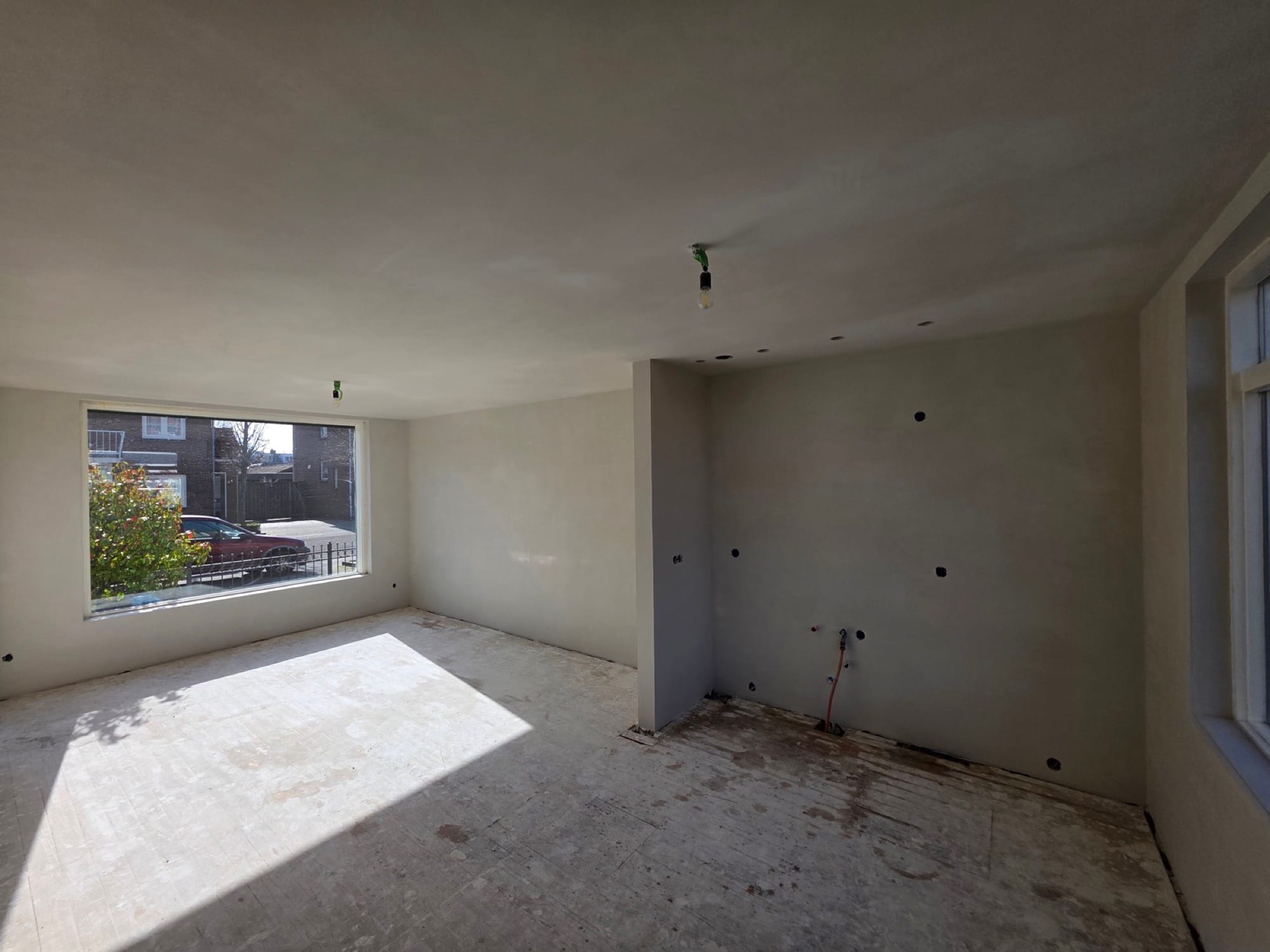Sausklare woonkamer in vol zonlicht met een strak gestuukte keukenwand