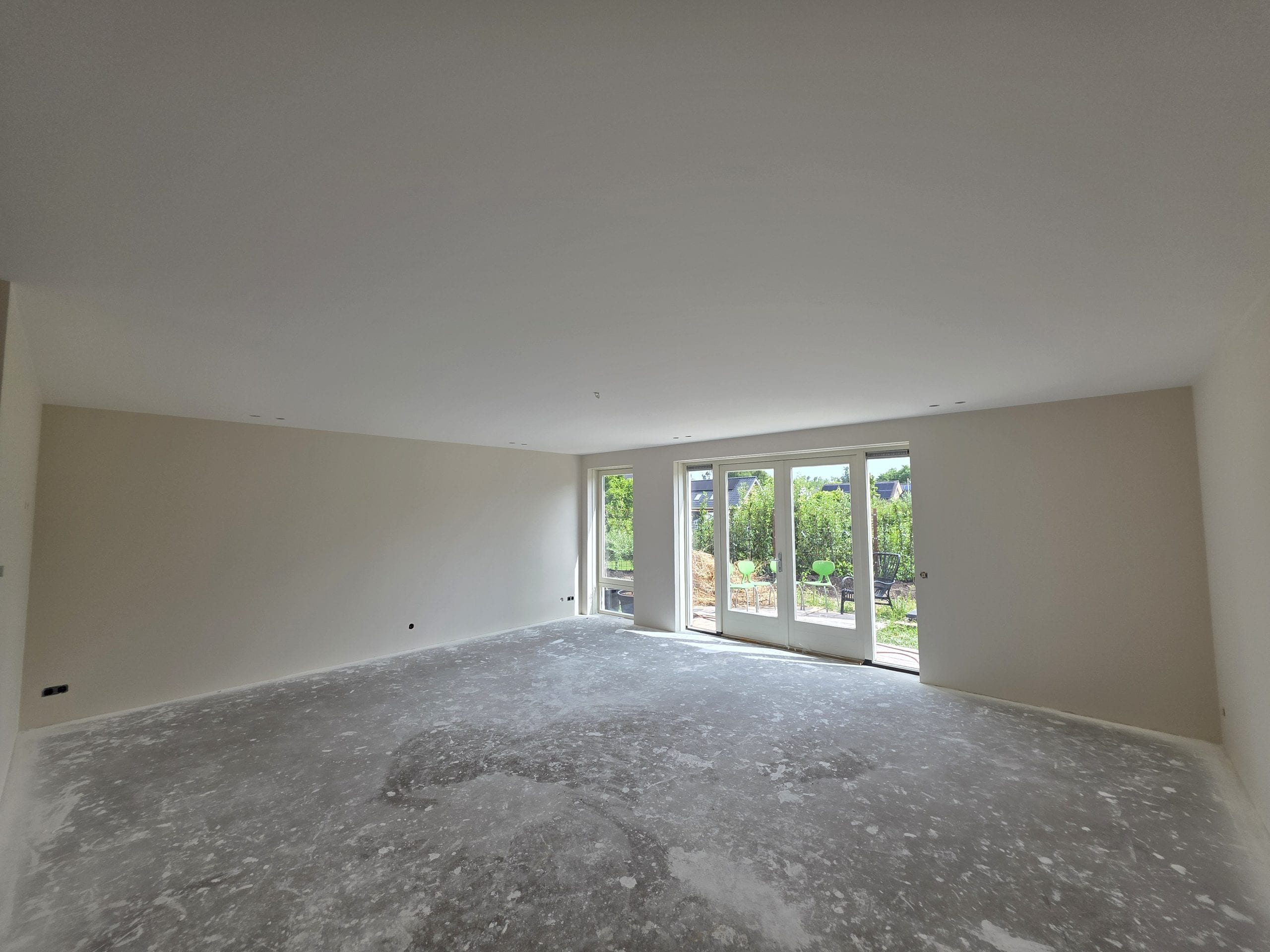 Ruime woonkamer met gladgestuukte wanden en plafond en een pui naar de tuin