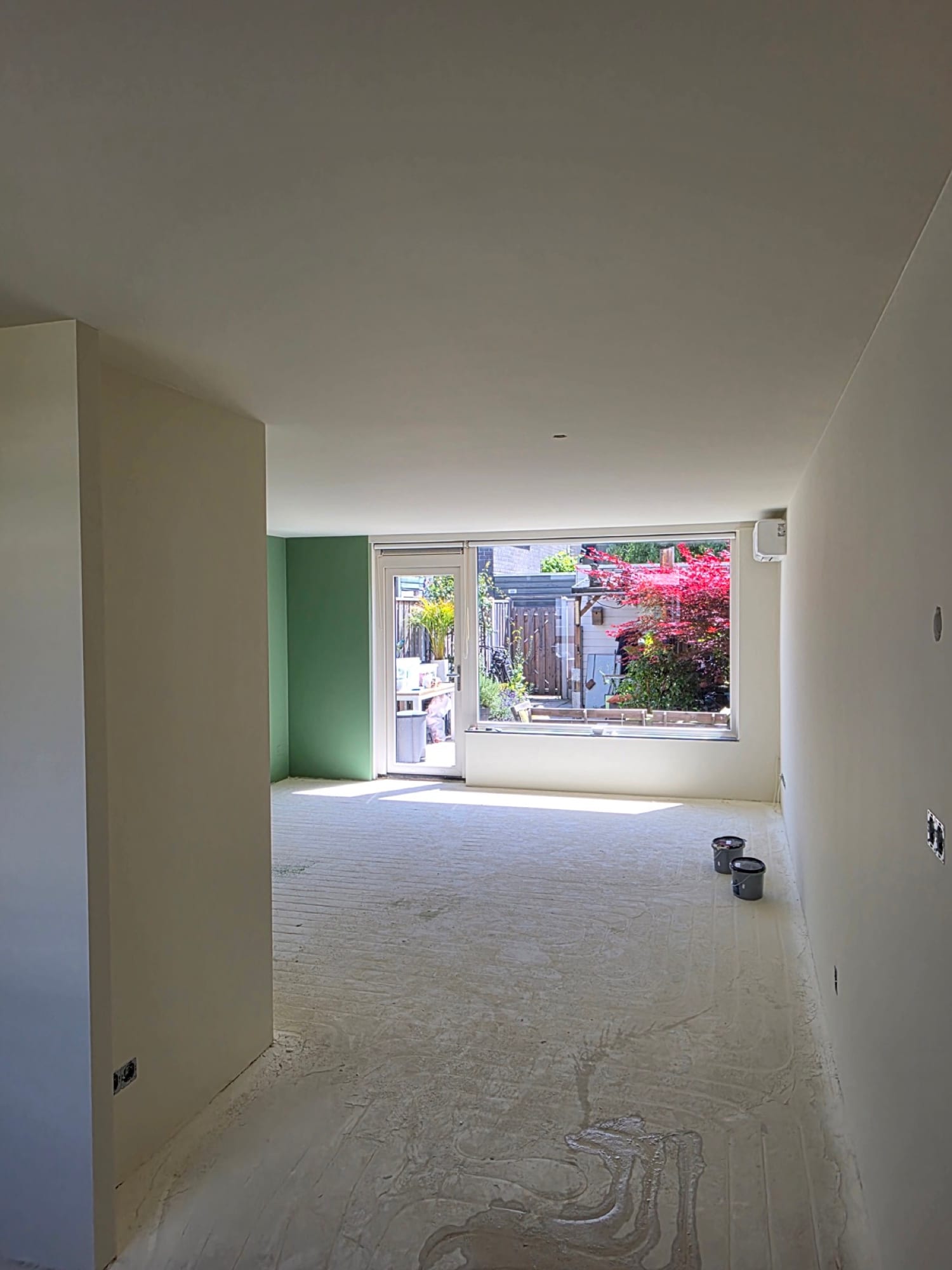 Afgewerkte woonkamer met groene accentwand en zicht op de tuin