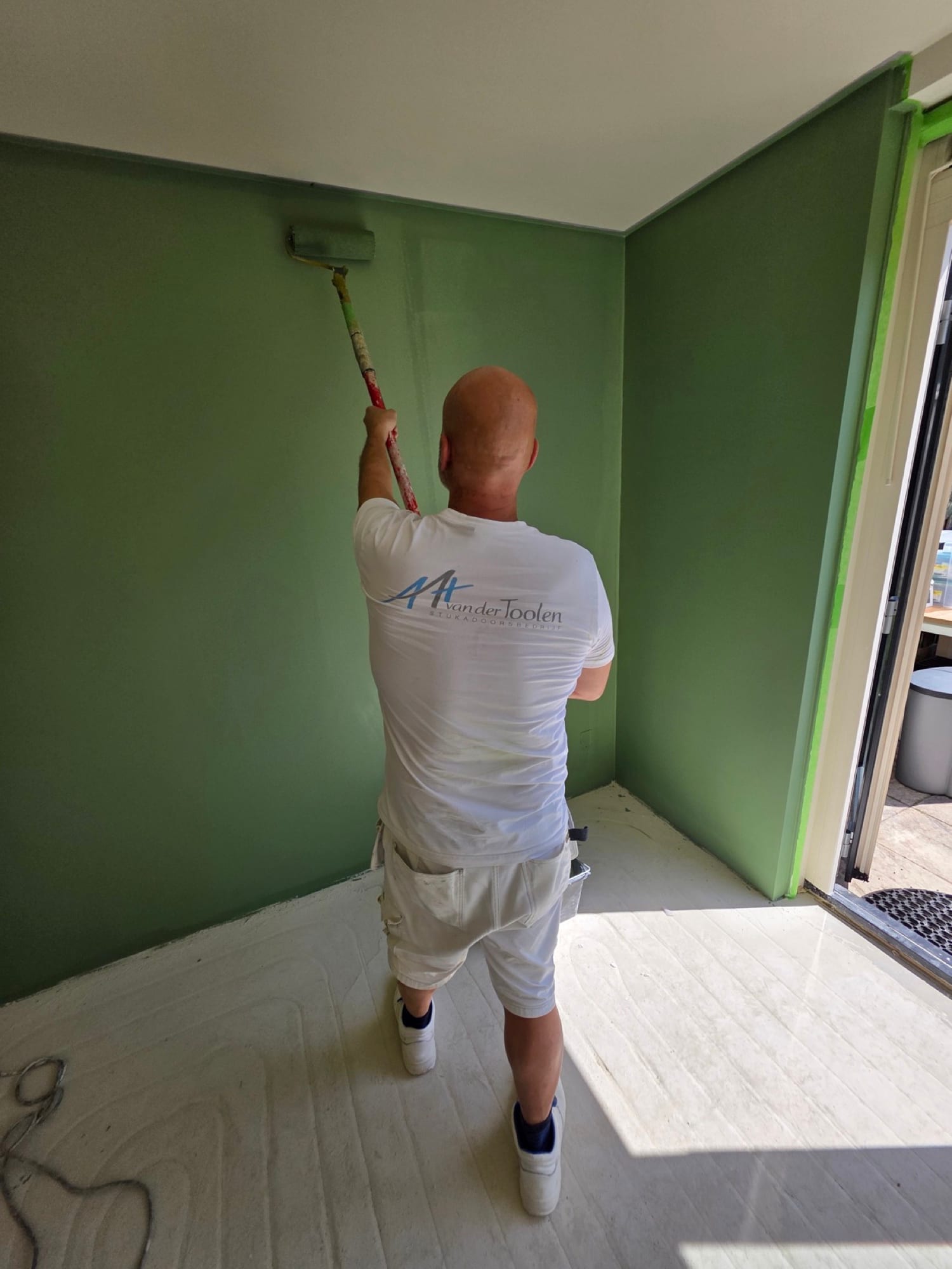 Stukadoor rolt groene muurverf over strak stucwerk