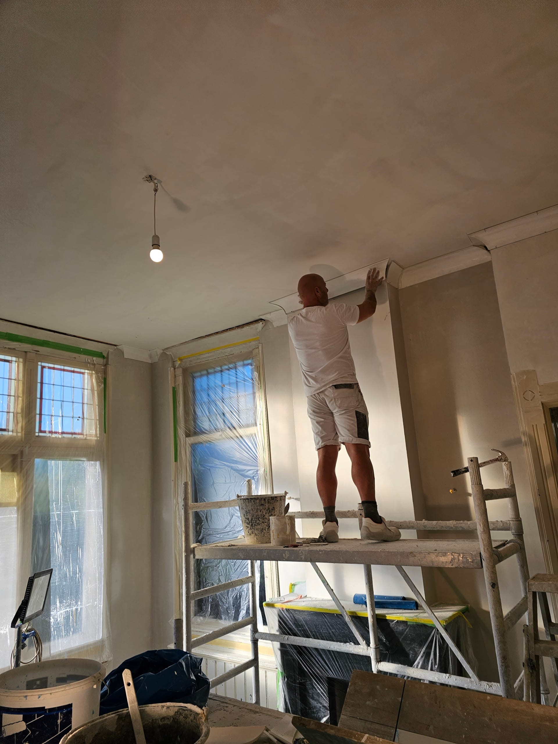 Rinaldi zet op de steiger een kroonlijst met de hand aan