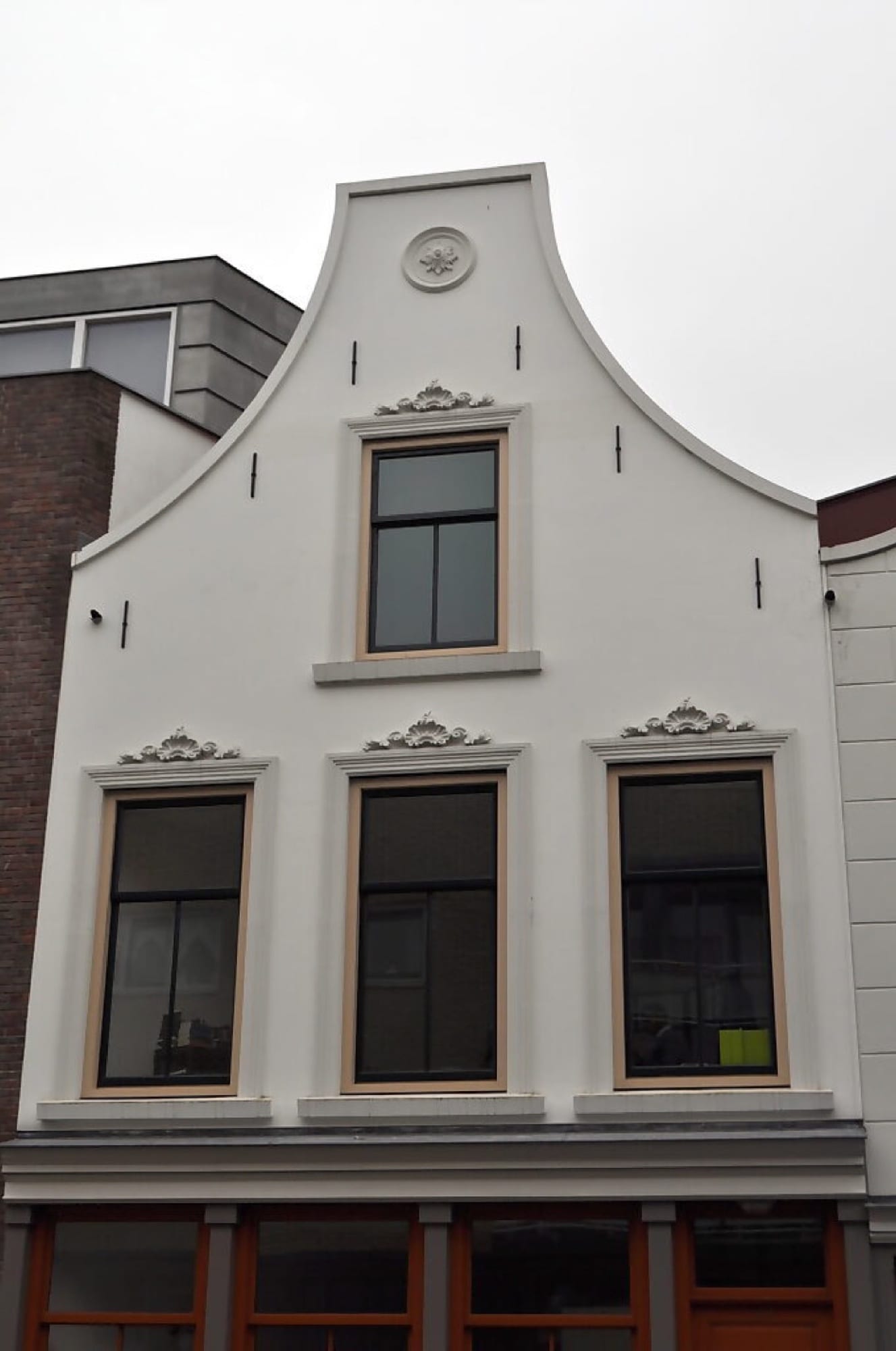 Glad gepleisterde klokgevel met sierornamenten, strak afgewerkt